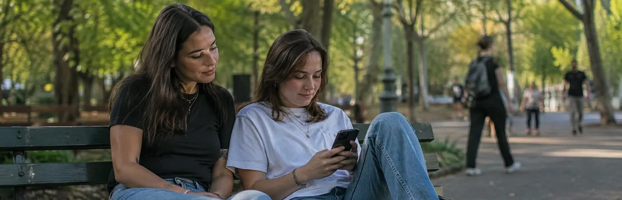 Two women looking at a phone while sitting on a park bench