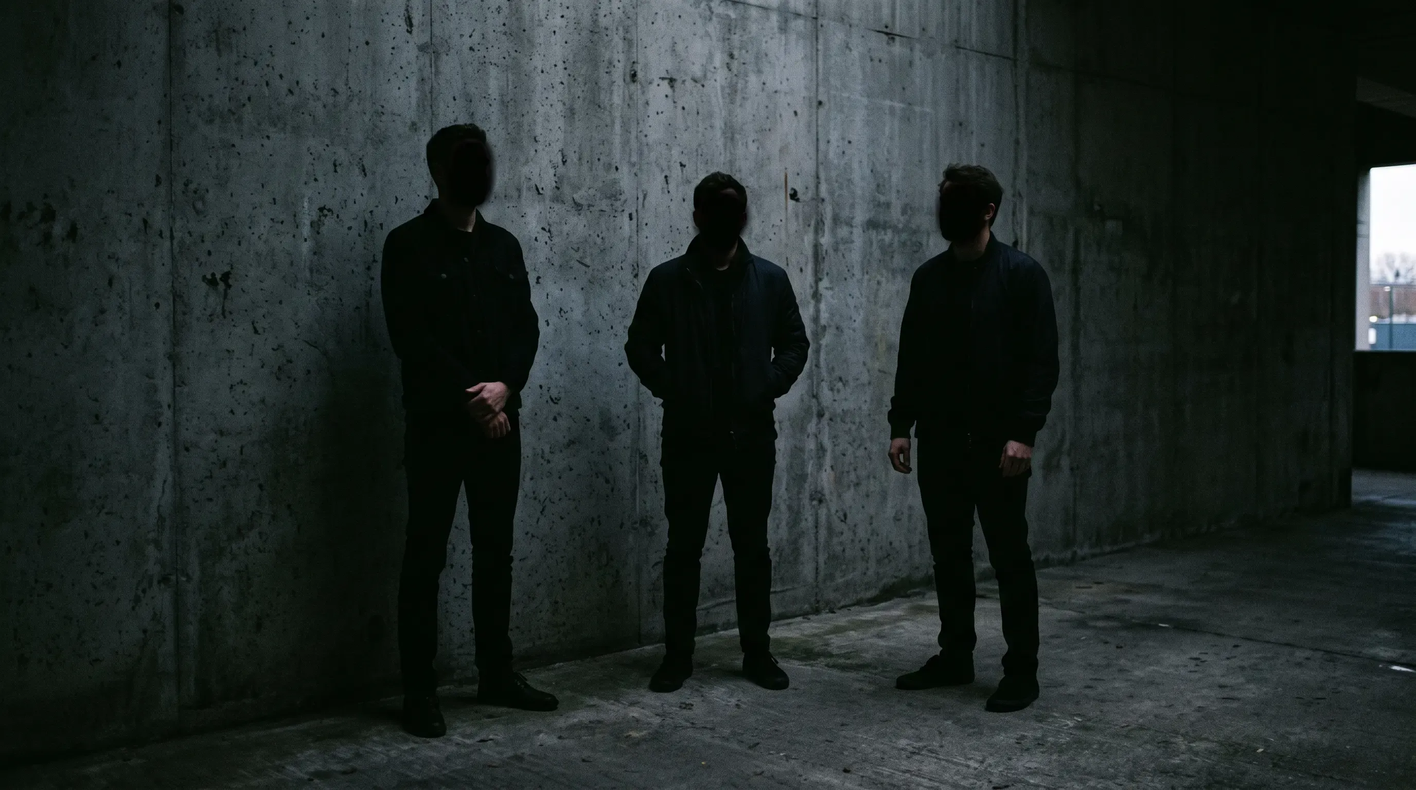 Three men standing in the dark against a wall.