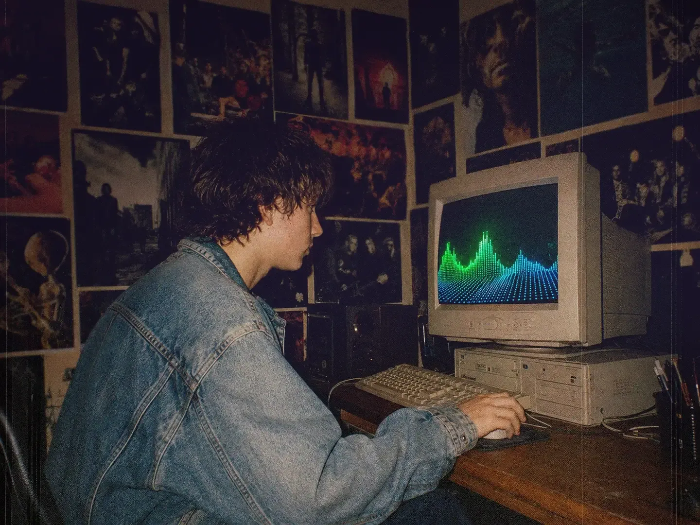 A young man in a denim jacket uses an old timey laptop