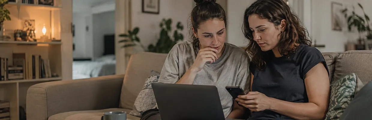 Two women on a couch using a laptop and a phone